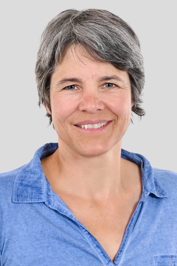 Eine Wissenschaftlerin und ein Wissenschaftler arbeiten hinter einer Glasfassade und mischen Chemikalien mit Großgeräten.