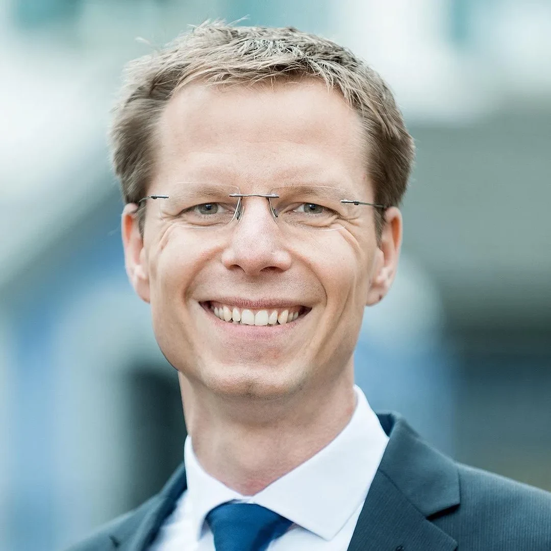 Eine Wissenschaftlerin und ein Wissenschaftler arbeiten hinter einer Glasfassade und mischen Chemikalien mit Großgeräten.